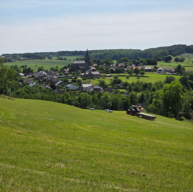 A large green field with a tractor and a town in the background