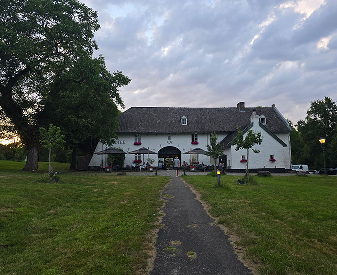A large, white, farm-style building with a gray roof, some umbrellas and greenery