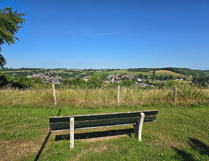 A wooden becnh on a viewpoint overlooking a green valley with a small town