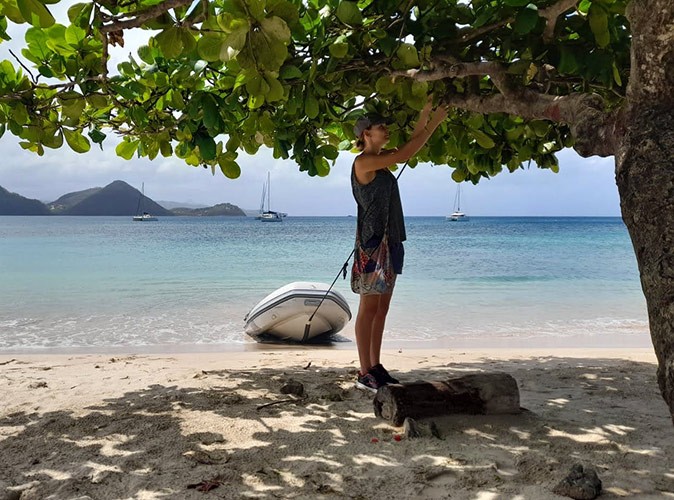 Life on a sailboat sailing around the Caribbean A woman tying a dinghy to a tree on a sandy beach