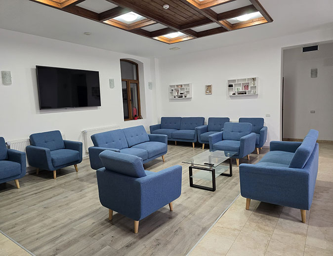 The communal living space in one of the hotels used during the nomad retreat Blue chairs and sofas in a bright space with a tv on the wall