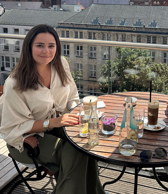 An expat living in Munich A woman with dark hair sitting at a round wooden table with a coffee