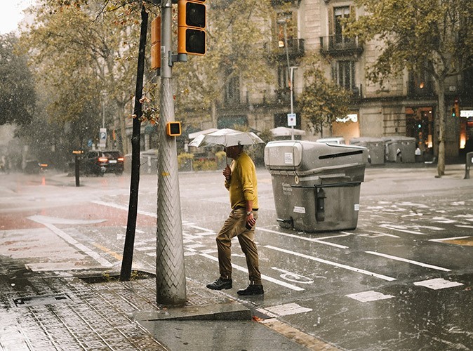 The weather in Spain A man with an umbrella crossing a city street in the rain
