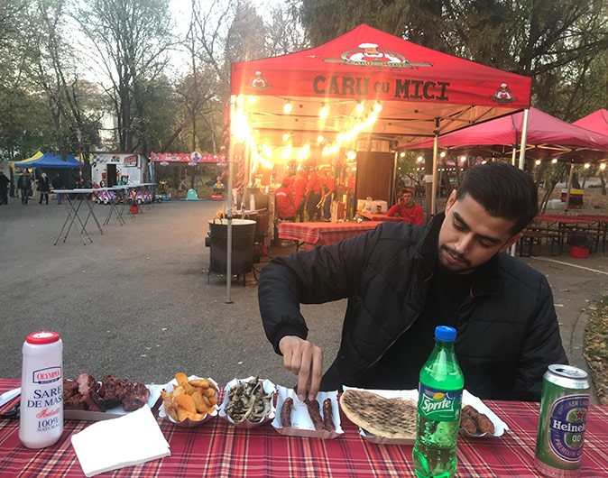 Moving to and living in Bucharest A man sitting at a table at an outdoor food fair with various small plates of food in front of him