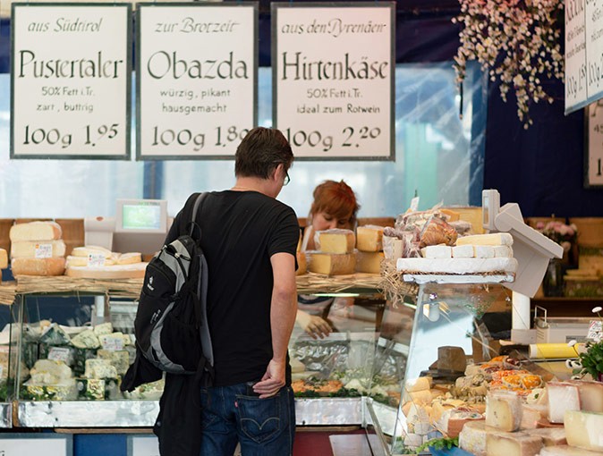 Life in Munich, Germany A man in a black tshirt looking at cheese behind a counter at a market stand