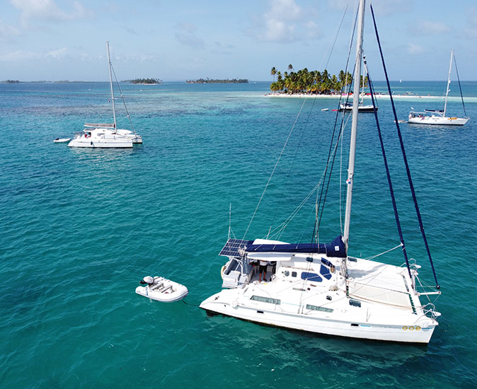 several sailboats anchored in crystal clear water with small tropical islands in the background