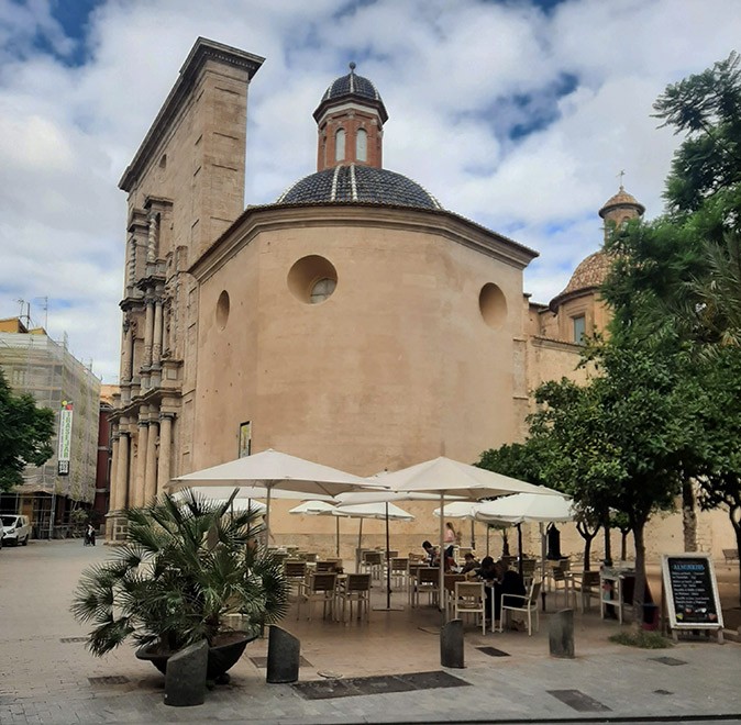 Living with noise in Spain A brown church building with a blue dome, on a square with a terrace with white umbrellas
