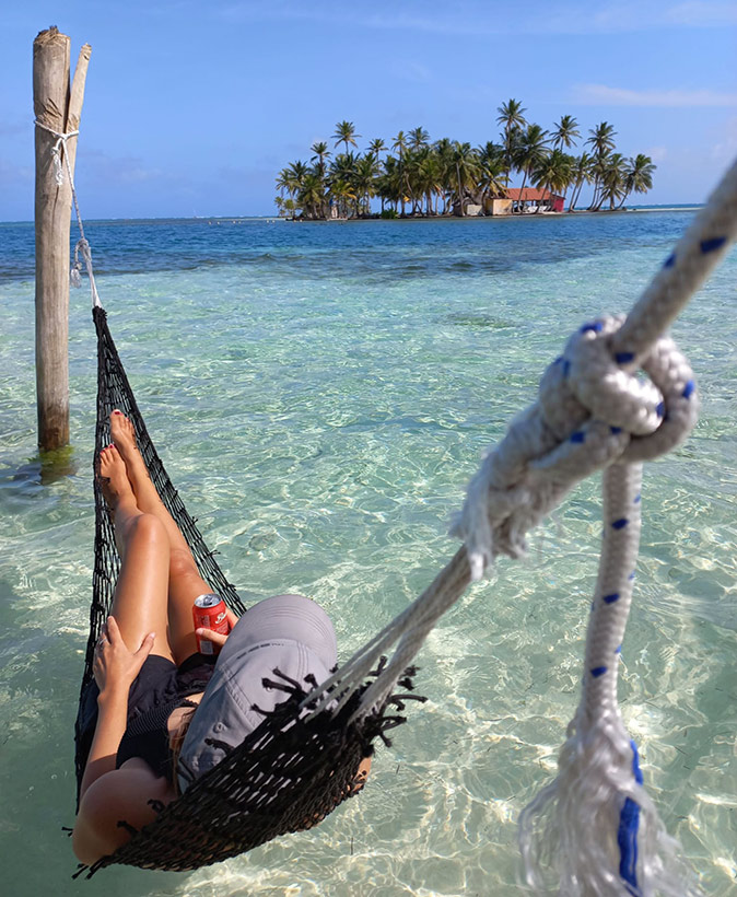A unique travel experience in Panama A woman in a hammock in crystal clear water with a small island with palm trees in the background