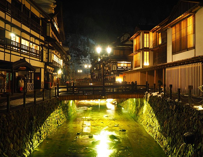 One of the best places in Japan to enjoy onsen A dimly lit street with a river in the middle, a bridge, and traditional Japanese houses on either side
