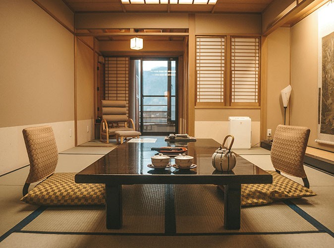 Japanese retreats A traditional Japanese tatami room with a low table with a tea pot and tea cups, floor cushions, and shoji screens.