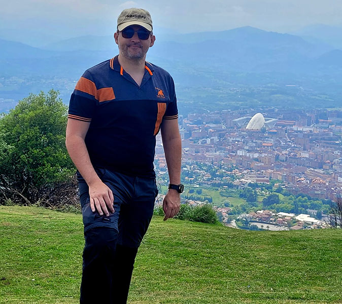 An expat living in Oviedo A man posing on a green hill with a city in the background