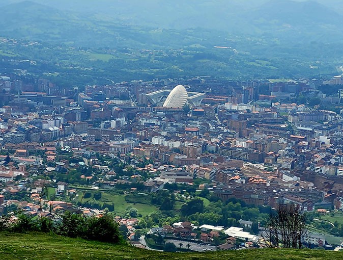 Life in Oviedo, Spain Aerial view of a city with a large modern looking building in the center, surrounded by mountains and greenery