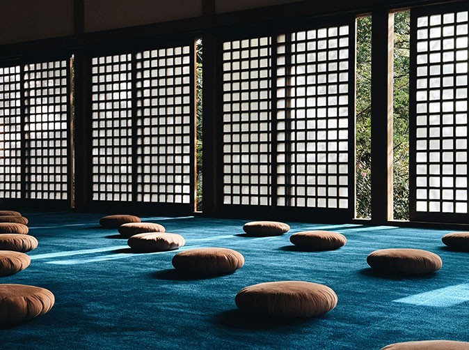 A meditation retreat in Japan Round, beige cushions spread out on a blue empty floor facing traditional Japanese sliding doors