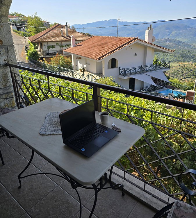 My experience working remotely with Tursi Digital Nomads A laptop on a table with a beautiful view of a valley with a couple of houses and greenery