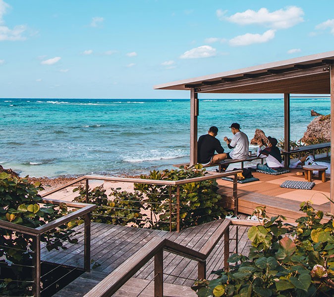 A seaside retreat in Japan Several people sitting on a covered terrace overlooking a bright blue ocean