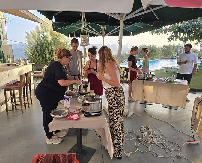 A cooking class as one of the activities organized by Tursi Digital Nomads Several people standing around tables with pans and small cookers at a cooking class in Greece