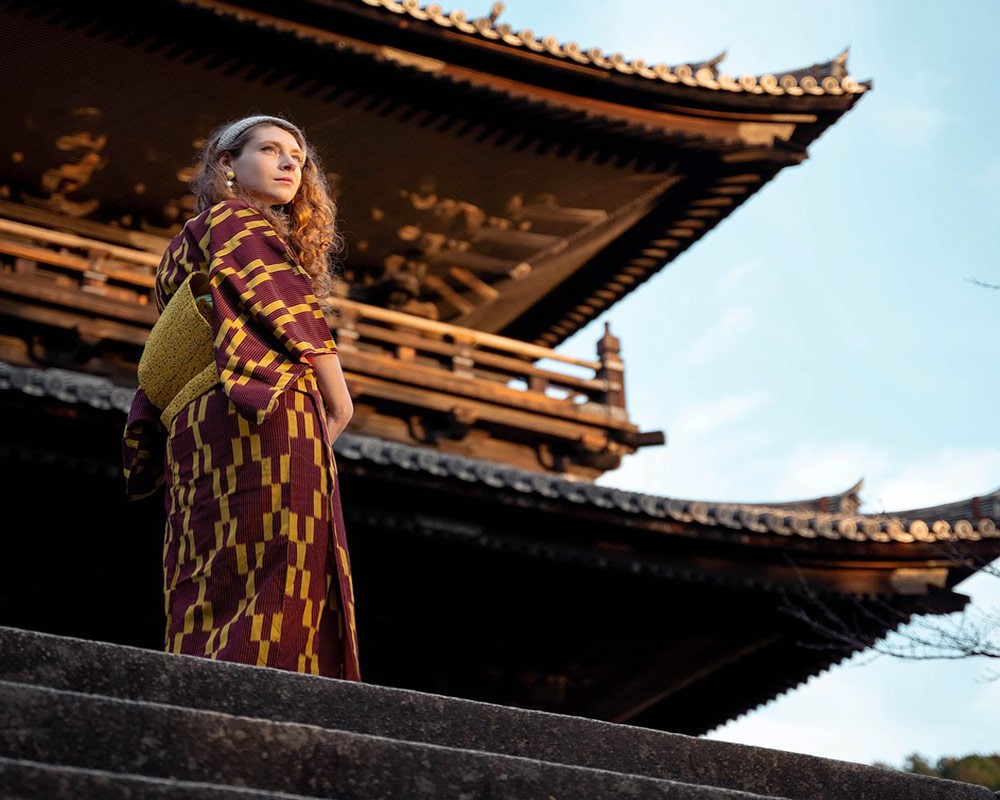 A blond woman in traditional Japanese dress standing in front of a temple