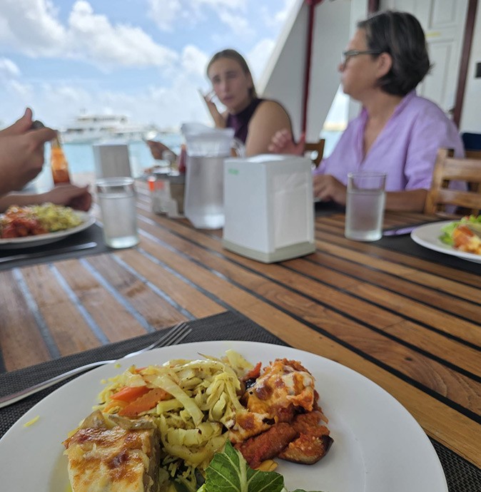 A wooden table on the deck of a boat with several plates of food and people sitting around it