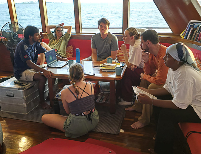 A group of people sitting around a dark table inside a boat