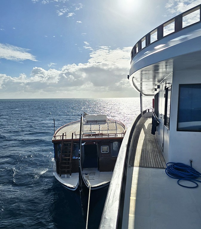 A small part of a large liveaboard in the right corner, with a traditional Maldivian dhoni tied next to it