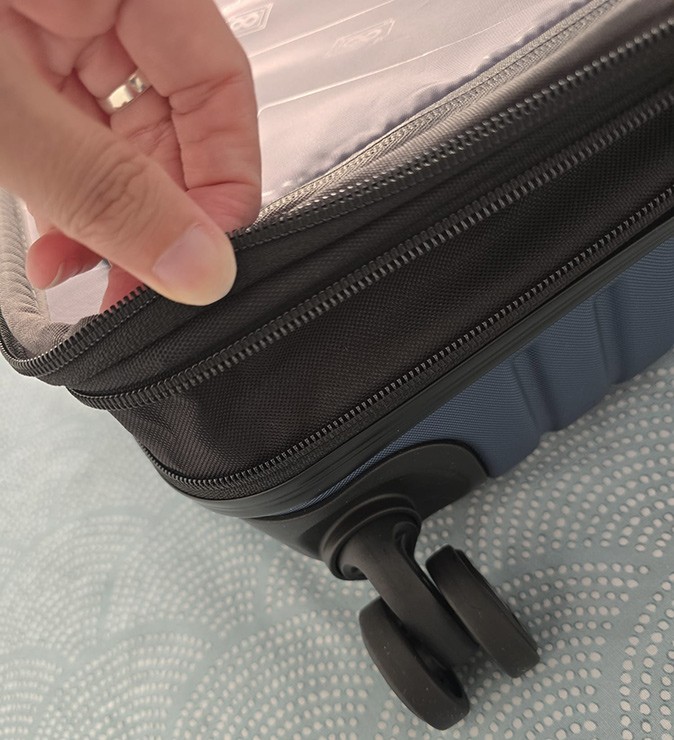 Carry-on luggage review A hand and a close-up of a suitcase showing zippers and one of the wheels