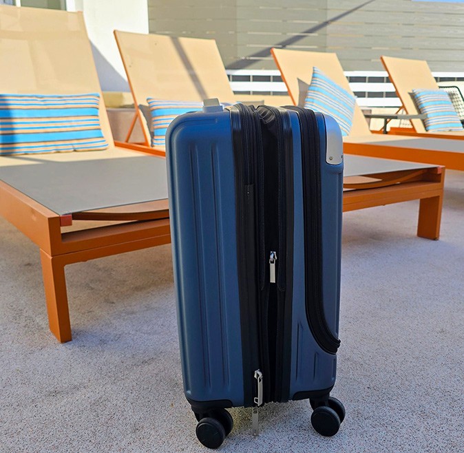 How to find the best carry-on suitcase A blue and black suitcase standing on the floor in front of several beige and orange sun loungers