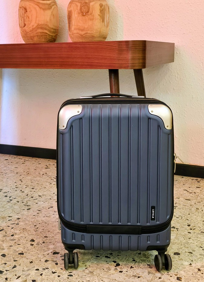 Important features of a good carry-on suitcase A sleek, blue and black suitcase standing on a speckled floor with a brown shelf in the background