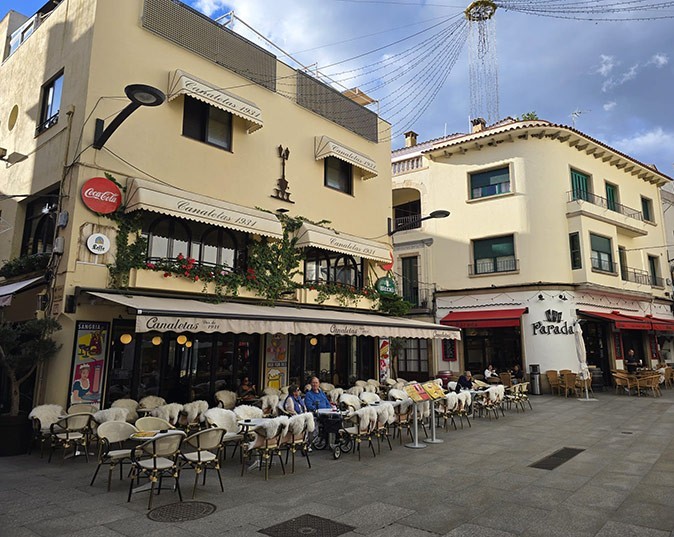 A beige building with a terrace in front of it with white tables and chairs and several people