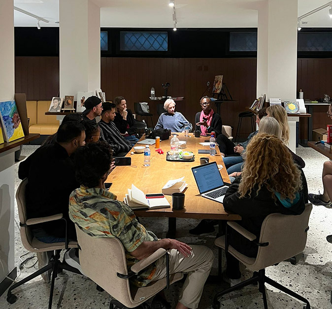 A group of people sitting around a wooden table, looking at one woman speaking