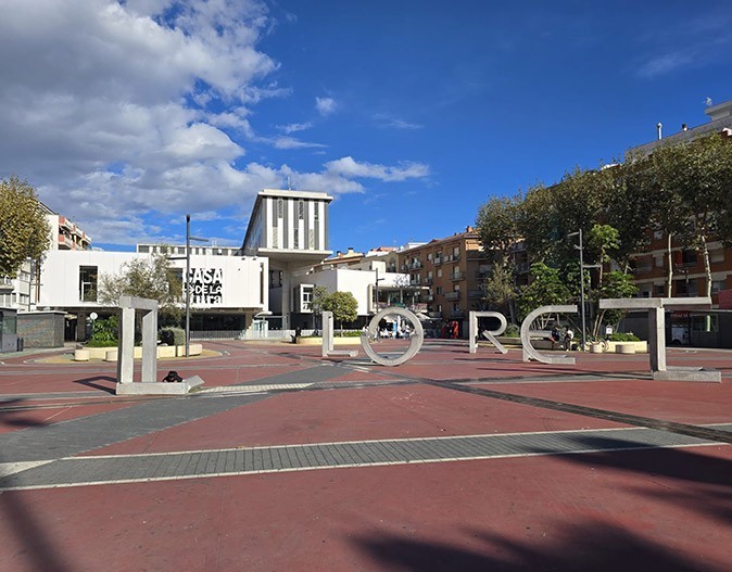 Large silver letters on a city square spelling "LLORET" with a modern white building in the background