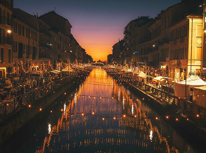 Christmas decorations at night, across a river in a city with festive looking market stalls on both sides