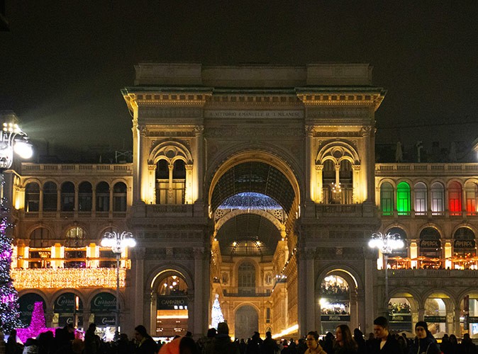 A brown historic mall at night decorated with Christmas lights and a crowd of people in front of it
