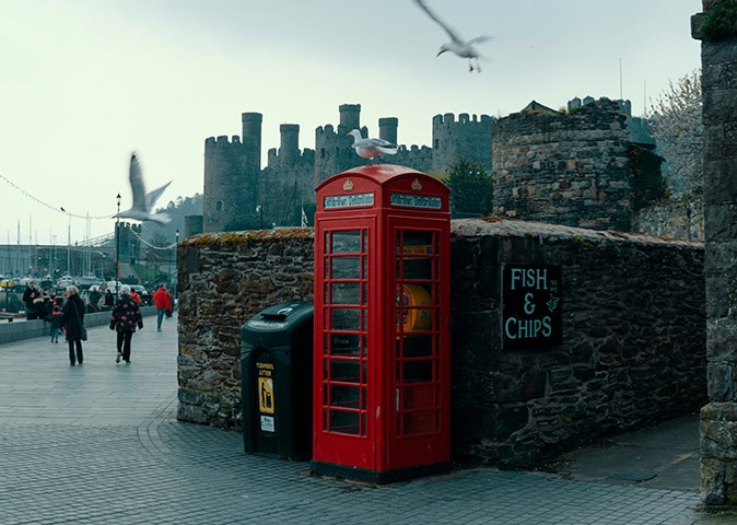 One of many castles worth visiting in the UK A typical British red phone booth standing in front of a castle with some people walking and some seagulls flying