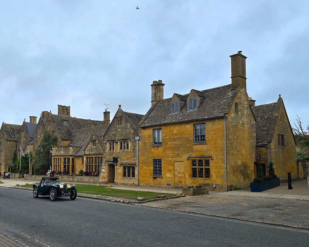 A row of typical British stone houses with a classic car passing in front of it