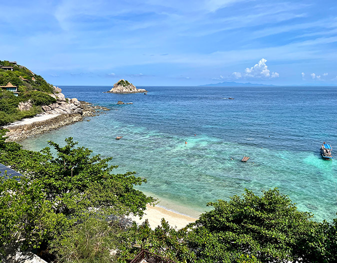 A tropical bay with white sand, bright blue water and greenery