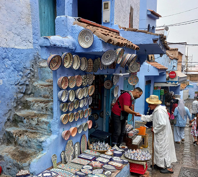 Friendly people in Morocco A pottery vendor standing in front of his white and blue painted store, surrounded by pottery, shaking the hand of an elderly man with a cane
