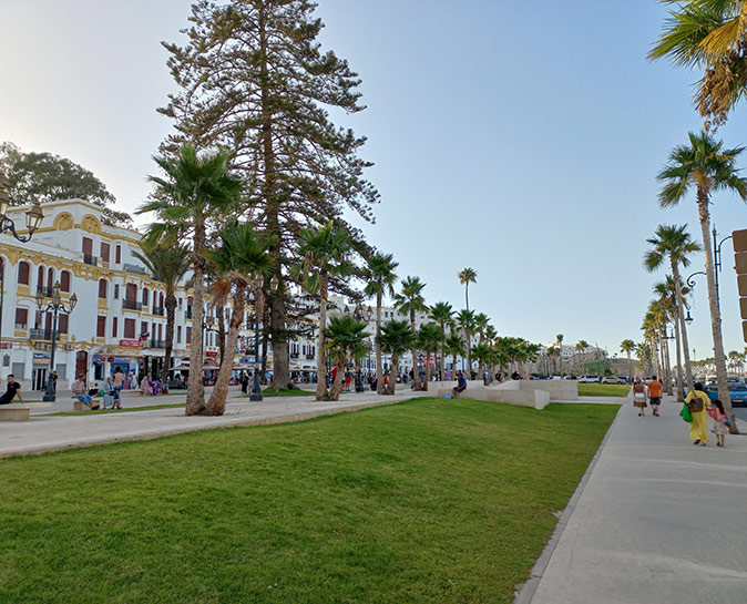 Living in Tangier, Morocco A well maintained grass field lined with trees, a boardwalk and white and yellow buildings in the background