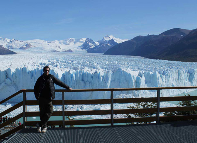 Places to visit in Argentina A man standing on a wooden deck in front of a large glacier