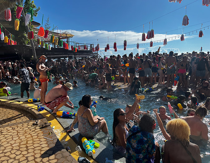 A pool party showing a pool with many people in and around it plus water guns and colorful decorations