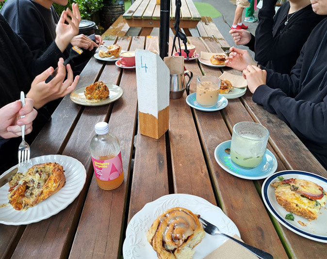 A wooden table with several pastries and coffees, showing only the hands and arms of several people sitting around the table