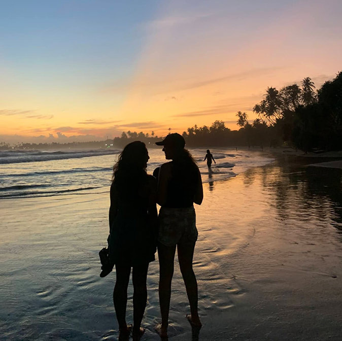 Enjoying life as a digital nomad in Sri Lanka Silhouette of 2 women standing on a sandy beach with the sunset and trees in the background