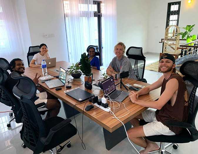 Several people sitting at a large wooden table with their laptops inside a coliving space