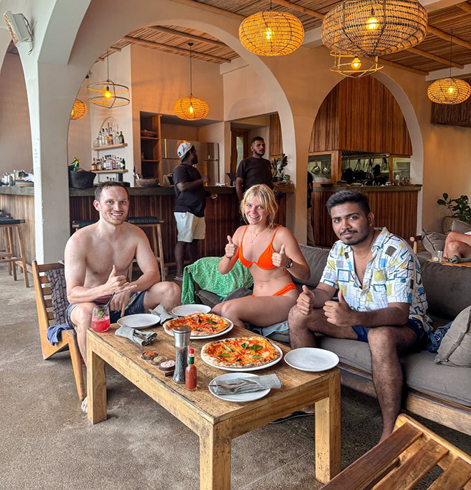 3 digital nomads in Sri Lanka 3 digital nomads sitting in a restaurant, smiling at the camera with food on a wooden table in front of them