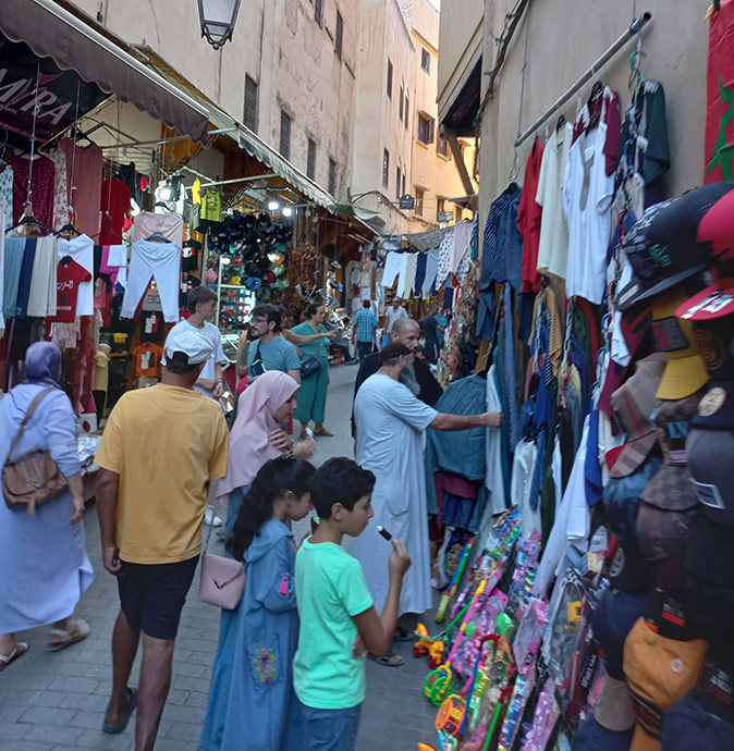 Life in Morocco A narrow street filled with pedestrians and several street vendors selling clothes and other items