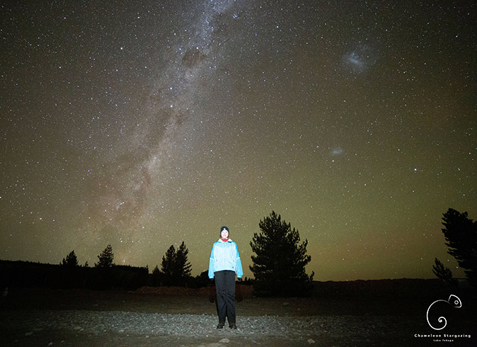 A woman in a lightblue coat, looking at the camera, standing under a bright starry sky showing the milky way