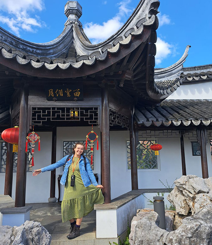A young woman in a green dress, smiling, standing in front of a Chinese pagoda