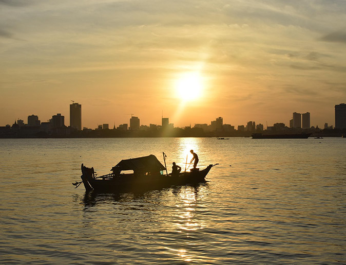 A Mekong River cruise in Cambodia Sunset over highrise buildings seen from the water with a small wooden boat in the foreground
