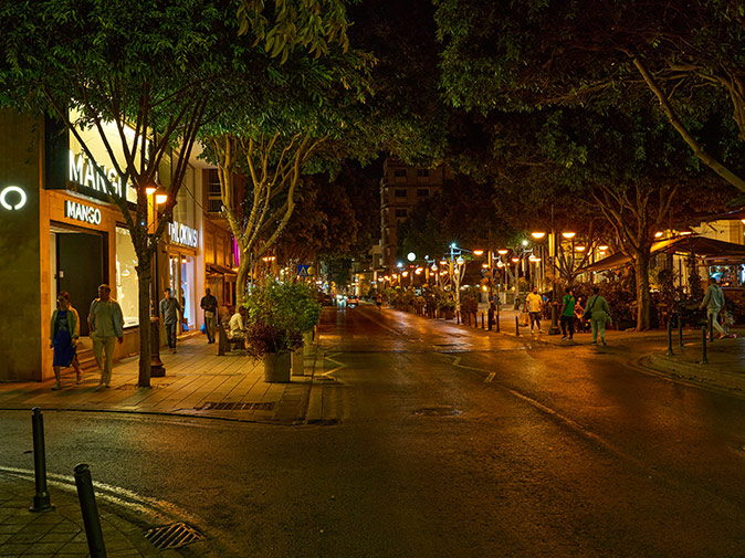 Limassol, a safe city to live in A wide, modern street at night, lined with shops and trees