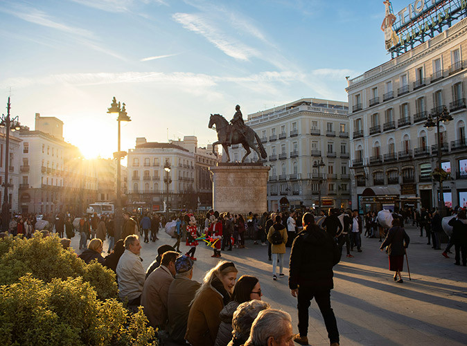 Tips for Living in Madrid A city square with many people, a large statue of a man on a horse, surrounded by white and gray buildings