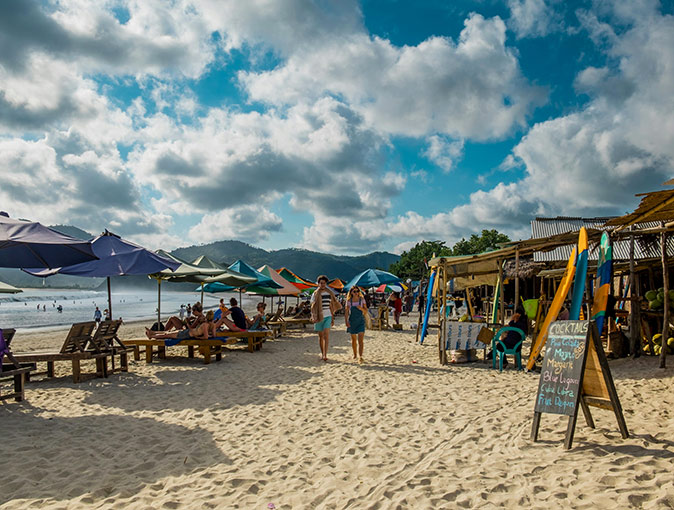 A popular coastal town to live in Lombok A sandy beach with many sun loungers and umbrellas, some people, shops and commercial signs